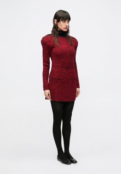 Červené dlhé šaty s textúrou, priliehavým strihom, zapínaním na predné gombíky a dvomi vreckami, v kombinácii s čiernymi pančuchami a balerínami.