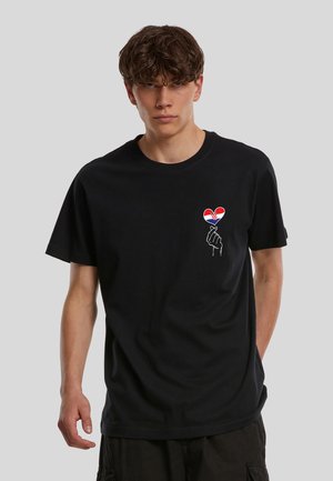Ung mand med krøllet hår iført en sort T-shirt med en hånd, der holder et hjerte med det kroatiske flag på brystet.