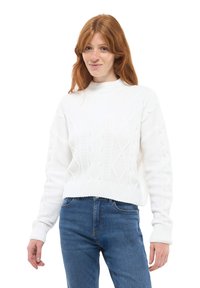 Biały sweter w splot kablowy z okrągłym dekoltem i ściągaczami u rękawów. Nosi się go na niebieskich dżinsach, co eksponuje fakturowe wzory na tkaninie.