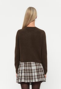 Καφέ πλεχτό πουλόβερ με στρογγυλή λαιμόκοψη, συνδυασμένο με φούστα καμπάνα σε καρό σχέδιο σε άσπρο, καφέ και μαύρο. Λείος υφασμάτινος ιστός, επίπεδο σχέδιο.