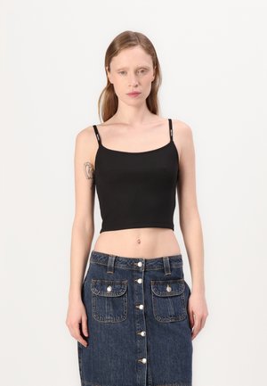 Črn crop top z tankimi naramnicami, rebrasto teksturo in okroglim izrezom, v kombinaciji z jeans krilom, ki ima sprednje gumbe in žepke.