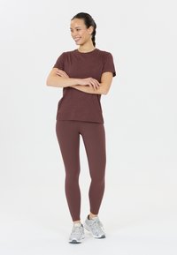 Körsbärsröd kortärmad skjorta i kombination med matchande körsbärsröda leggings. Modell som bär ljusgrå sportskor. Slät material, figurnära design.