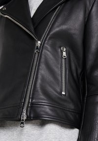 Giacca da moto in pelle nera con design corto, cerniere in argento e finitura testurizzata. Presenta una tasca laterale e un colletto asimmetrico.