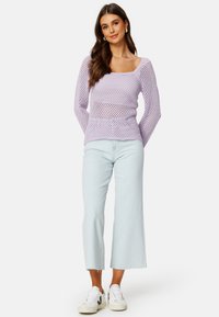 Maglione leggero viola chiaro a maglia aperta con maniche lunghe abbinato a jeans corti blu chiaro e sneakers bianche con accenti neri.