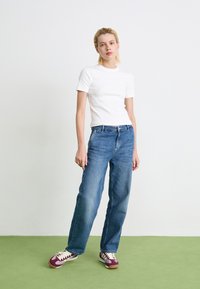 Hvid kortærmet skjorte, blå straight-leg jeans og mørkerøde sneakers med hvide detaljer. Simpelt, afslappet outfit med en løs pasform.