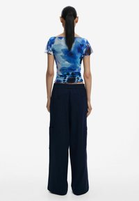 Top a maniche corte, blu e bianco con stampa astratta, realizzato in tessuto leggero, abbinato a pantaloni cargo comodi di un blu scuro con tasche laterali.