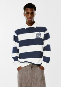 Polo majica dugih rukava s tamnoplavim i bijelim horizontalnim prugama, od pamučnog materijala, i malim izvezenim logom na lijevoj strani.