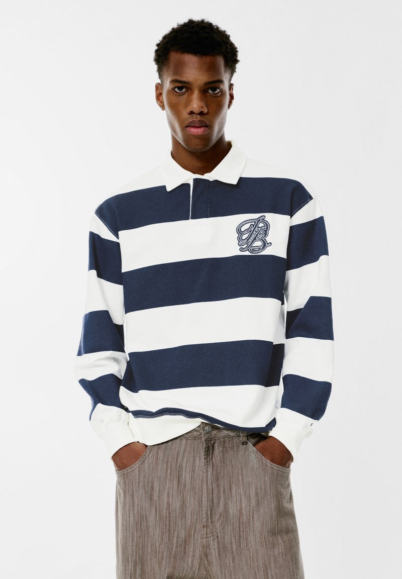 Polo majica dugih rukava s tamnoplavim i bijelim horizontalnim prugama, od pamučnog materijala, i malim izvezenim logom na lijevoj strani.