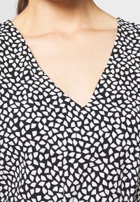 Black dress with a deep V-neck, featuring a white abstract pattern of small shapes across the fabric. Soft, lightweight material.