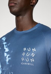 Blå atletisk skjorte med rund hals, teksturert stoff og en logo med teksten "RUN" og "ICANIWILL" i hvitt.