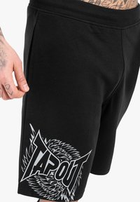 Černé sportovní šortky vyrobené z měkké látky, s výrazným bílým grafickým designem a textem "TAPOUT" s ostrými akcenty.