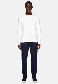 White cotton sweatshirt with round neckline, long sleeves, ribbed cuffs, paired with navy pants and black sneakers with white soles.