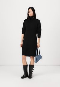 Black knit turtleneck dress, knee-length, with long sleeves. Paired with a light blue handbag and black knee-high boots featuring buckles.