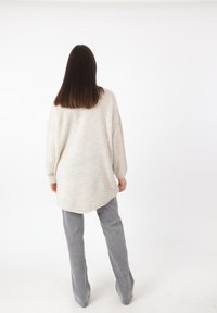Maglione lavorato a maglia di un beige chiaro e texture, con vestibilità ampia e maniche lunghe, abbinato a pantaloni dritti grigi chiari. Lunghezza standard, con dettagli minimi.