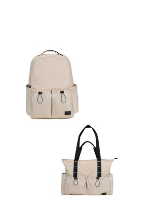 Mochila beige con bolsillos delanteros y bolso tote beige con asas negras, ambos con cierre de cordón y un pequeño parche con logo negro.