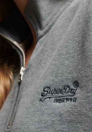 Close-up van een grijze sweatvest met rits, voorzien van het zwarte geborduurde "SuperDry"-logo en Japanse tekens op de borst.