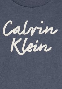 Heather marine t-skjorte med rund hals og teksturert hvit skrift som staver "Calvin Klein" over forsiden.