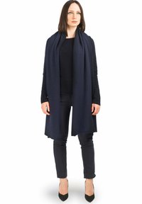 Sciarpa di lana blu scuro con una texture liscia, disposta in modo elegante, abbinata a un top scuro e pantaloni neri attillati. Tacchi a punta neri completano l'outfit.