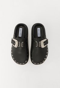 Black clogs with a sleek design, textured leather material, prominent silver buckle accent, and metal stud detailing around the sole.
