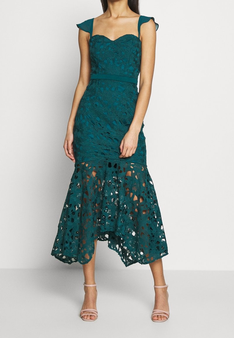 Abito in pizzo teal con maniche a previsto, corsetto aderente e orlo svasato con dettagli a taglio. Tessuto liscio con motivi floreali.