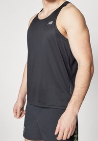 Svart atletisk linne med ribbat mönster, rundad halsringning och liten logotyp på vänster bröst, matchat med mörka träningsshorts.