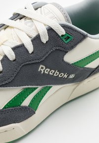 Grå och krämfärgade sneakers med gröna accenter, i mocka och läder, med strukturerad yta, snören och en synlig Reebok-logotyp.