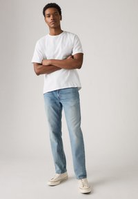 T-shirt branca de algodão com mangas curtas, combinada com jeans de ganga azul clara e ténis brancos; design minimalista, corte descontraído e textura suave.