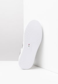 Biała podeszwa sneakersów z teksturowanym wzorem grip, z małym logo i detalem włoskiej flagi. Gładkie krawędzie i minimalistyczny design.