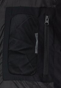 Tissu de veste noire avec une poche en maille et une poche zippée. La texture est lisse avec un design léger adapté à l'empilage.