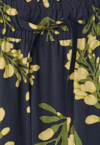 Tissu foncé avec imprimé botanique vert et jaune, doté d'une taille froncée et d'un cordon noué au centre.