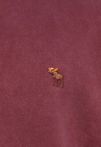 Sweat-shirt bordeaux avec une finition texturée, présentant un petit orignal brodé avec des bois sur le côté gauche.