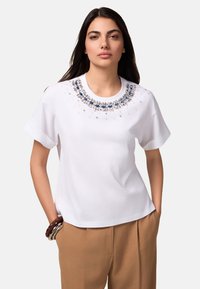 Witte t-shirt met korte mouwen, voorzien van een met juwelen versierde halslijn versierd met blauwe en heldere kralen, gladde stof en een ontspannen pasvorm.
