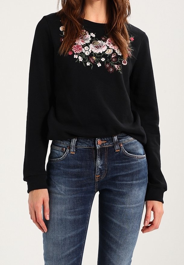 Sweatshirt noir avec broderie florale en rose, blanc et bordeaux. Associé à un jean en denim à lavage moyen. Texture douce, coupe décontractée.