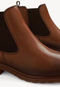 Paire de bottines Chelsea en cuir marron avec panneaux latéraux élastiques et languettes de tirage sur fond blanc.