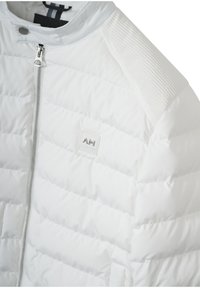 Giacca puffer bianca con texture trapuntata, colletto rialzato e zip frontale. Accentuata da spalle rigate e una piccola etichetta con logo.