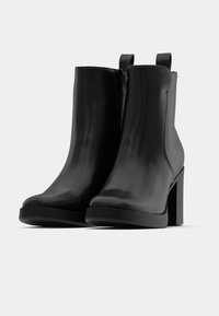 Bottines noires en cuir lisse, talons épais hauts, fermetures éclair latérales, et languettes à l'arrière pour un enfilage facile.