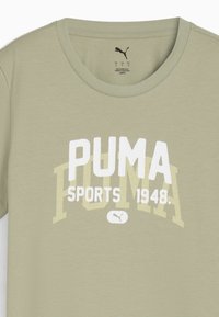 Camiseta de algodón verde oliva claro con mangas cortas, cuello redondo y un gráfico de texto en blanco y amarillo "PUMA SPORTS 1948".