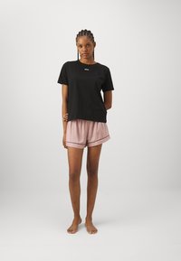 Black cotton t-shirt with white "BOSS" logo, paired with light pink satin shorts featuring a contrasting trim. Model standing barefoot.