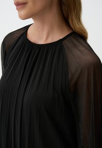 Zwarte geplooide blouse met doorzichtige lange mouwen, een gathered halslijn en een gladde textuur. Het ontwerp heeft vloeiende stof zonder patronen.
