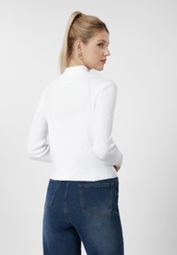 Camisola branca de malha canelada com gola alta e mangas compridas, combinada com jeans de cintura alta azul escuro com bolsos traseiros.