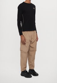 Černé tričko s dlouhým rukávem a malým logem, béžové cargo kalhoty s pokrčenou texturou a bočními kapsami, doplněné černými teniskami.