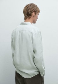 Chemise en lin vert clair à manches longues, col traditionnel et fermeture à boutons. Texture lisse, ourlet arrondi et coupe décontractée.