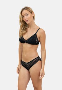 Soutien-gorge en dentelle noire et culottes assorties avec motif géométrique, comportant des bretelles réglables et un détail de nœud central sur le soutien-gorge.
