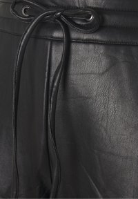 Pantalons en cuir noir avec taille à cordon. La texture est lisse avec une légère texture grainée, et le design comprend des détails de couture le long des coutures.