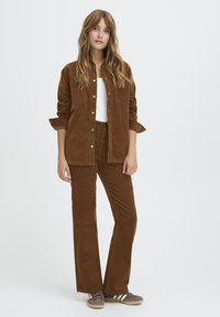 Brown corduroy shirt and matching flared pants, paired with a white top and brown sneakers, featuring a button-up design and textured fabric.