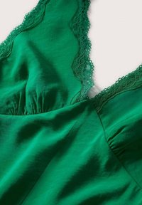 Robe en tissu vert soyeux avec bordure en dentelle le long du décolleté en V et détails froncés au niveau de la poitrine.