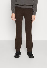 Pantalons tricotés marron avec une coupe slim, présentant une texture lisse et une taille élastique. Assortis à des baskets noires.