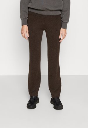 Pantalons tricotés marron avec une coupe slim, présentant une texture lisse et une taille élastique. Assortis à des baskets noires.