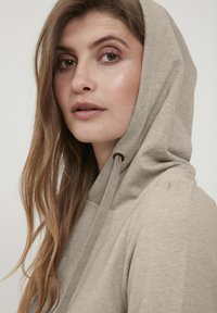 Svetlo bež sweatshirt s kapuco in vrvico, mehkega tekstura, z sproščenim dizajnom in minimalnimi šivi.