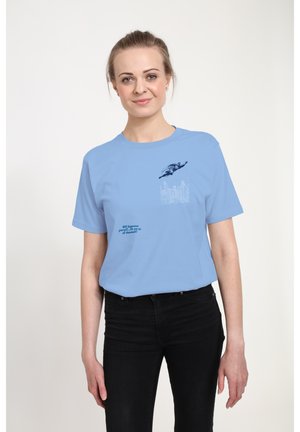 Lyseblå bomulds t-shirt med et grafik af en flyvende superhelt og tekst i mørkeblå, sat mod en enkel baggrund.